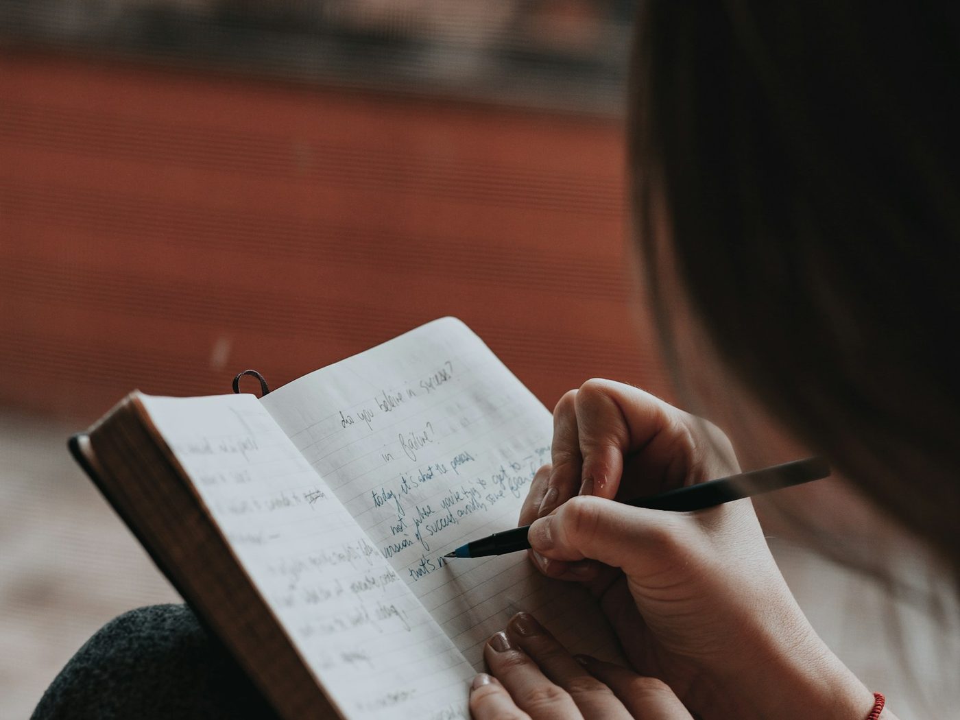 A person writing observations by hand in a notebook, warm natural light.