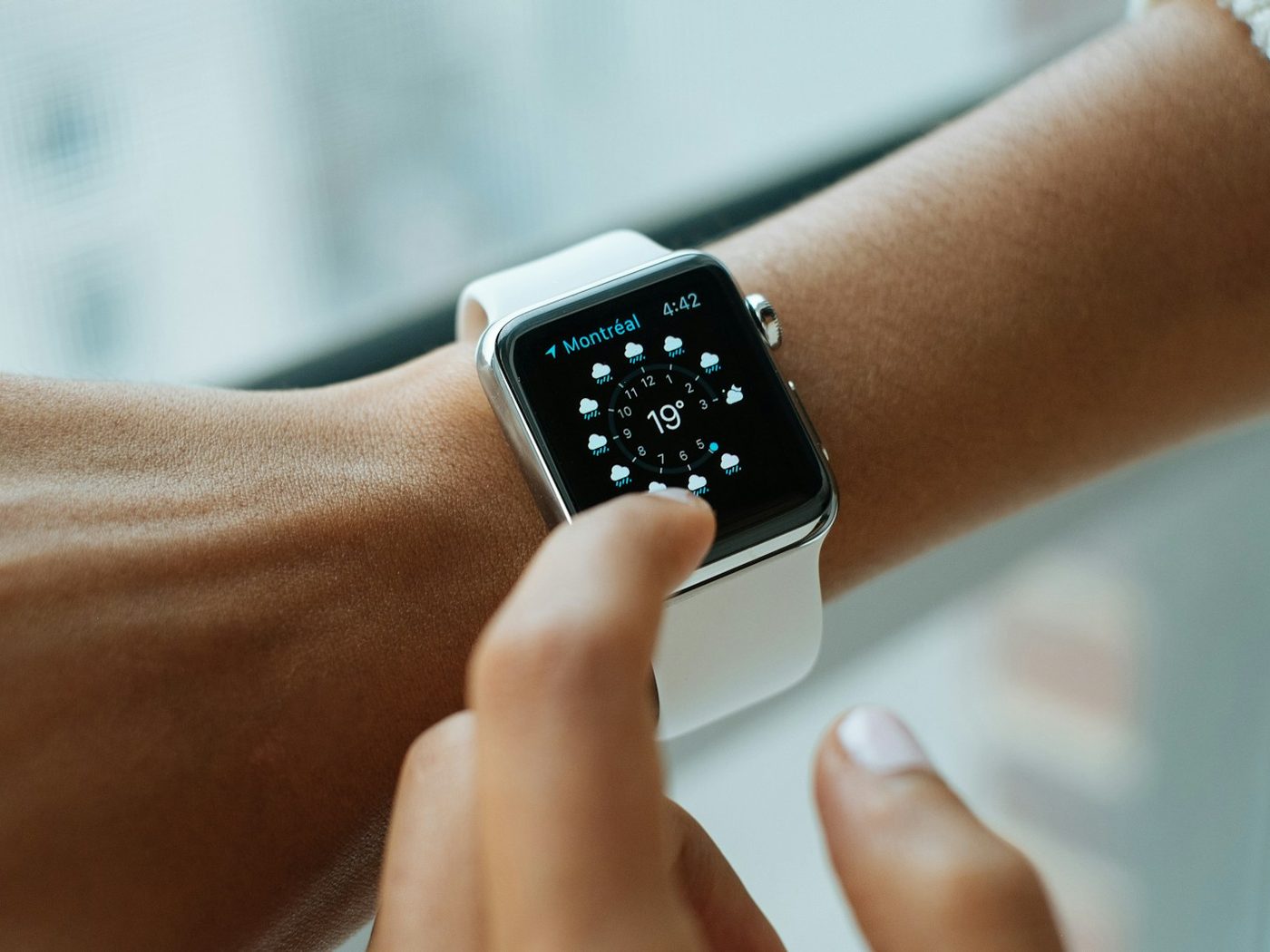 A person checking a smartwatch on their wrist, mid-tap on the screen, natural window light.